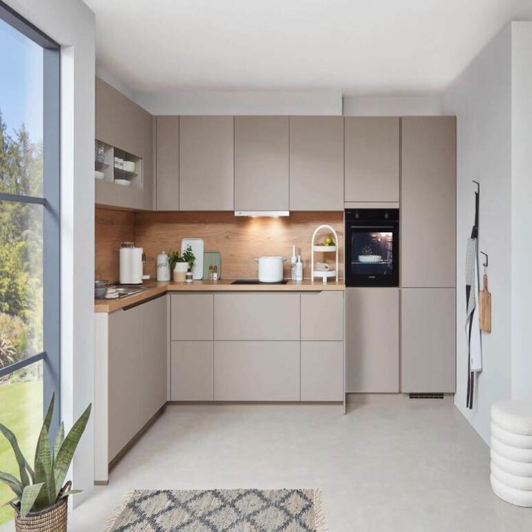 Musterküche in Kaschmir als L-Küche mit Holzrückwand und Backofen im Hochschrank – Küchenstudio Offenbach